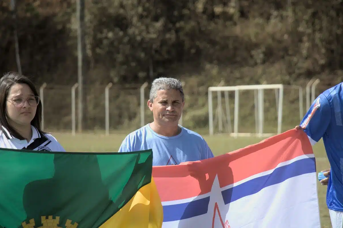 No centro da foto, Aloísio Caburé, presidente da Liga Esportiva de Mariana, segura a bandeira da entidade, tendo ao seu lado ua mulher que segura a bandeira de mariana, na abertura do campeonato de futebol amador de Mariana