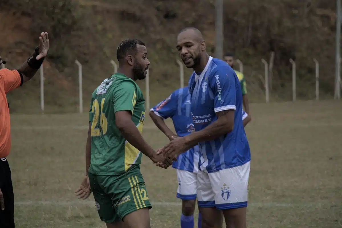 Ao final do jogo, Hudson, do 8 de Dezembro, com camisa verde, faixa diagonal em amarelo no peito e número 26 às costas, cumprimenta o atacante Dudu, do São Caetanense, usando calção branco e camisa azul