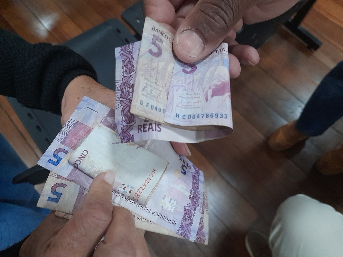 Mãos de pessoas com notas de cinco reais, recolhidas como vaquinha para a aquisição de lanche durante o segundo congresso das associações de moradores de Mariana