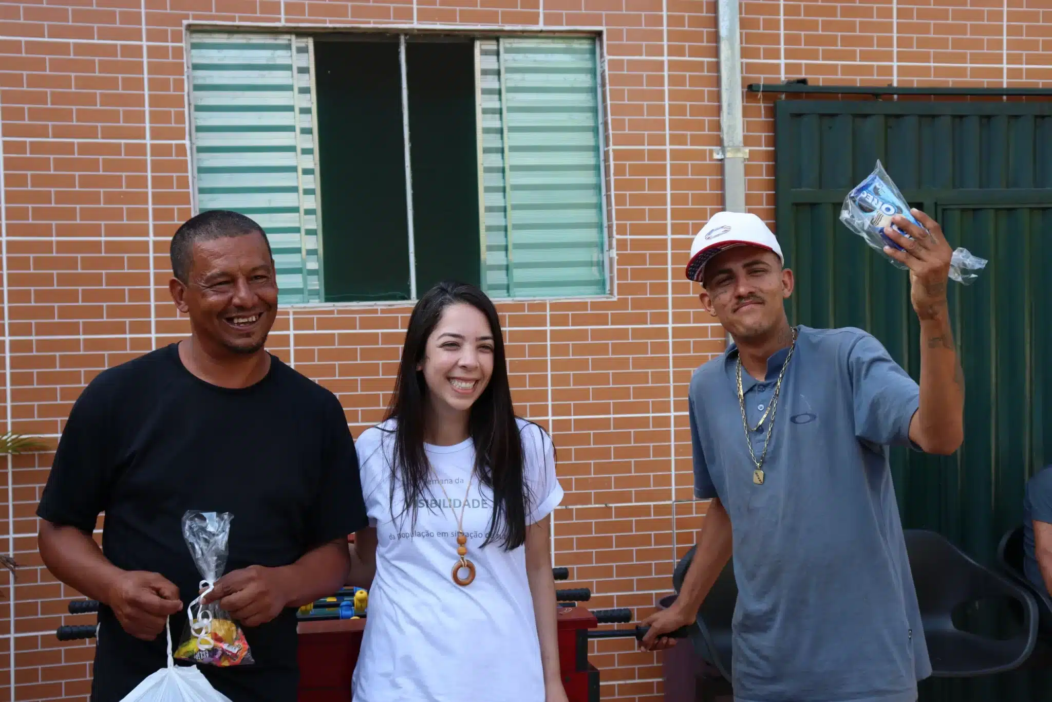 Vinicius Costa e Genivaldo Magno, com a coodenadora do Centro Pop, Paola Araújo dos Santos, sorriem e exibem os prêmios de 1º e 2º lugar do campeonato de totó