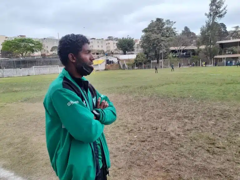 Feijão, técnico das categorias de base do América, à beira do campo com jogadores mirins ao fundo