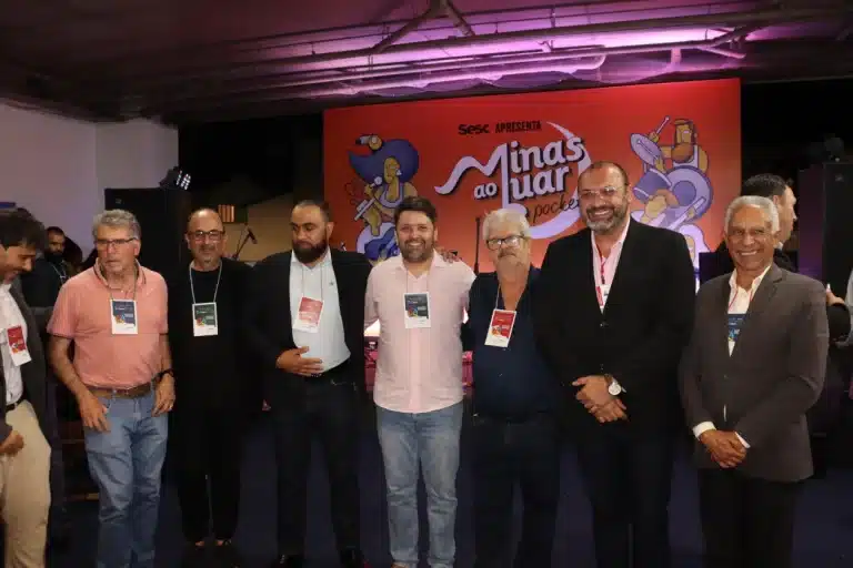 Autoridades posando para foto em frente a um cartaz do Minas ao Luar, na abertura da 2ª Semana de Desenvolvimento Econômico de Mariana