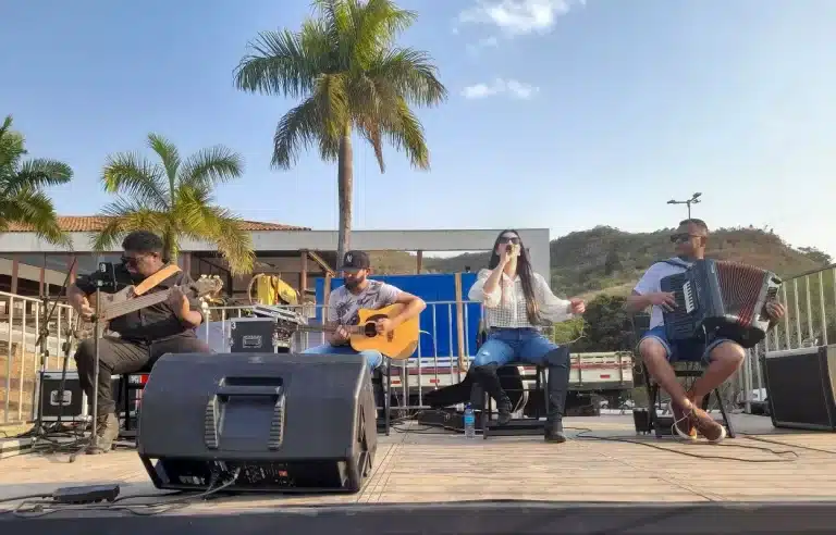 No palco, músicos tocando baixo, violão e sanfona, acompanham cantora em show durante o 1º Feirão de Automóveis de Mariana