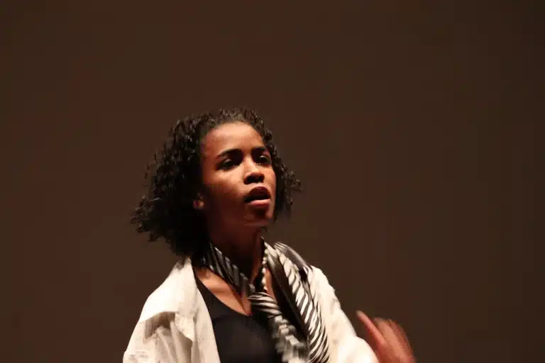 Dançarina apresentando-se na noite de abertura da 6ª edição do Festeco, de cabelos cacheados, usando camisa branca aberta, gravata com listras em preto e branco