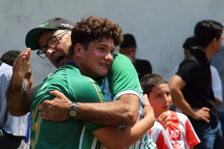 Homem de óculos e bone, cumprimenta efusivamente um atleta mirim, com camisa verde, depois do título conquistado pelo Guarany, na categoria sub-15, nas finais do campeonato de base em Mariana