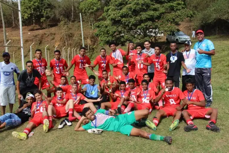 Jogadores do Olimpic, de uniforme vermelho e branco, posam para foto de comemoração do título da categoria sub-17, conquistado no último jogo das finais do campeonato de base,juntamente com integrantes da comissão técnica. À frente, deitado, o goleiro da equipe, usando uniforme verde
