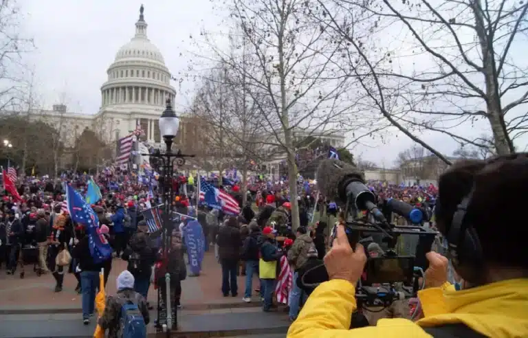 Diante do Capítólio, manifestantes são filmados por cinegrafista, em primeiro plano, à direita, usando roupa amarela, em ato considerado contrário à democracia