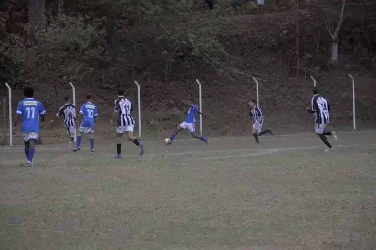 Jogador do São Caetanense, de calção branco e camisa azul, domina a bola, cercado por jogadores do União, de calções também brancos e camisas em preto e branco.