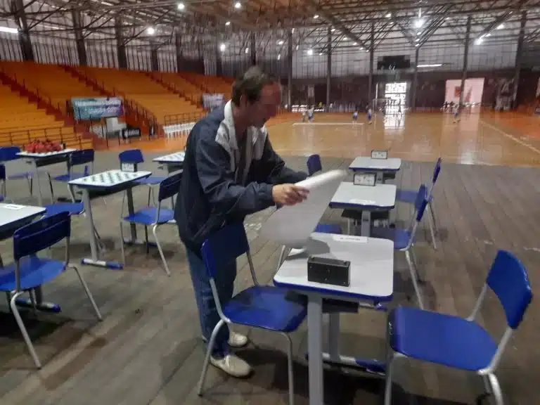 Árbitro da competição de xadrez dos Jogos Escolares de mariana recolhe os materiais utilizados nas mesas colocadas no palco da Arena Mariana