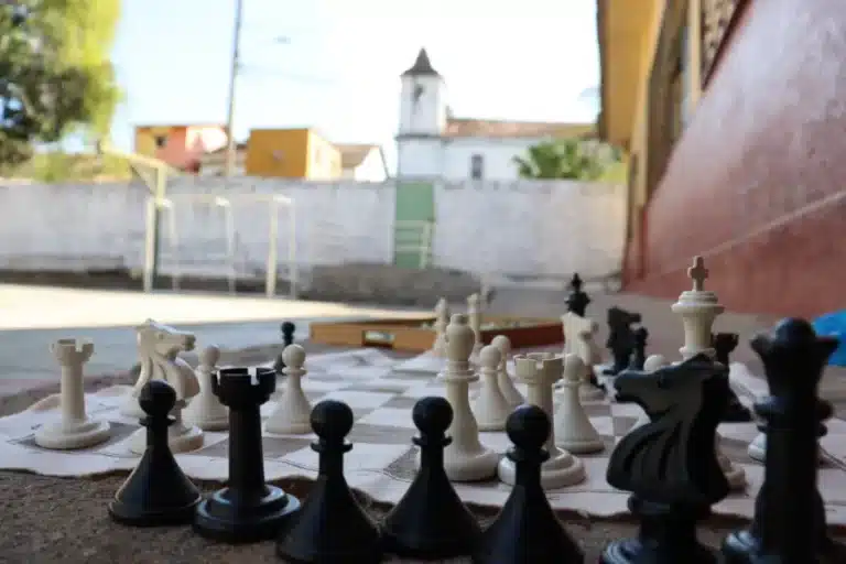 Em primeiro plano, tabuleiro de xadrez, colocado no chão do pátio da Escola Monsenhor Morais, com algumas peças brancas e pretas