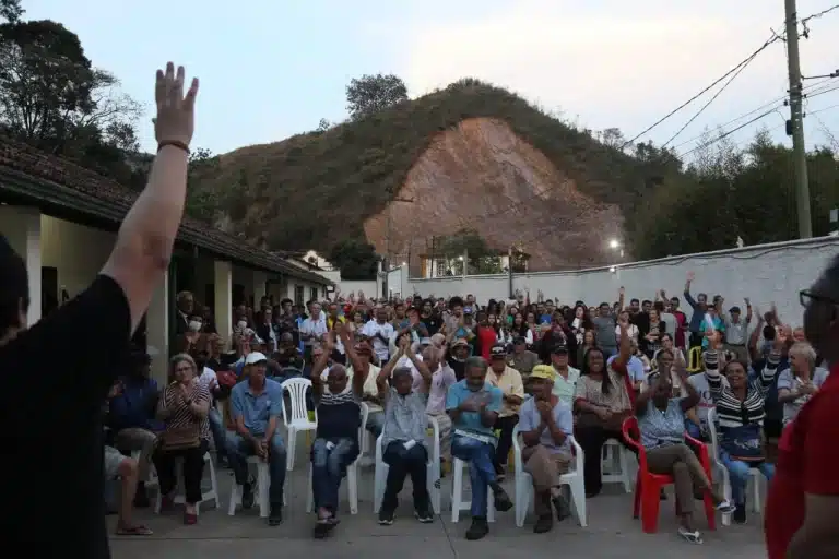 Em um pátio, pessoas participam de assembleia popular e votam por desobediência civil em relação à cobrança de água pelo consumo
