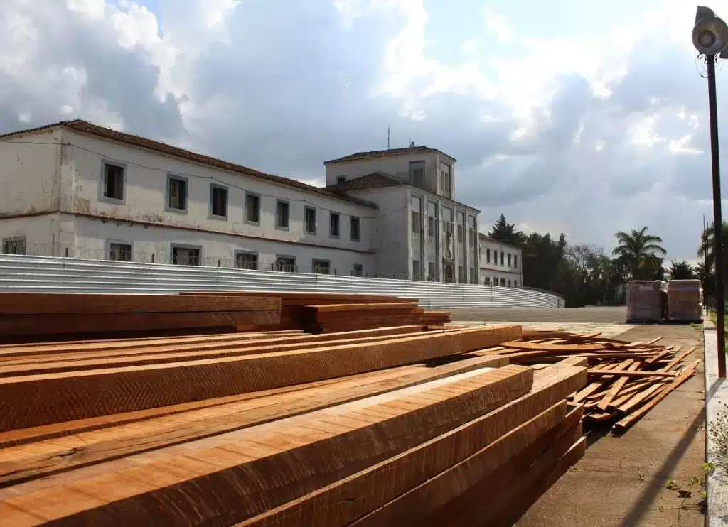 Ao fundo, fachada do Colégio Dom Bosco, cercada por um tapume de metal, em fase de restauro, com madeiras amontoadas em primeiro plano
