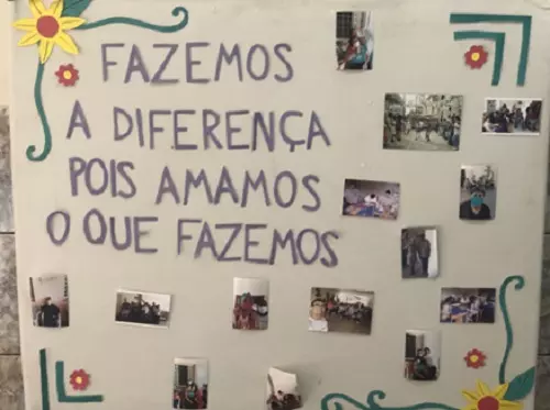 Cartaz com fotos, em uma parede da Comunidade da Figueira., com a legenda: "Fazemos a diferença pois amamos o que fazemos"