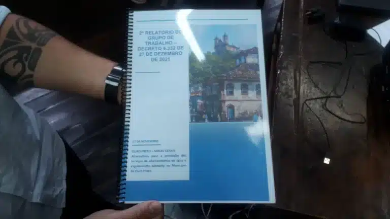 Mão exibindo a encadernação do relatório que recomendu a remunicipalização dos serviços de água e esgoto em Ouro Preto