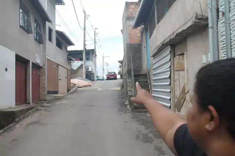 Em uma rua estreita e íngreme do bairro Alto do Rosário, mulher aponta para casas que têm problema de abastecimento de água