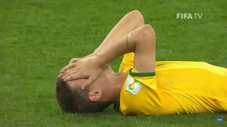 Jogador Oscar, com camisa amarela, deitado no gramado do Mineirão, lamenta a desclassificação da Seleção Brasileira nas semifinais da Copa de 2014