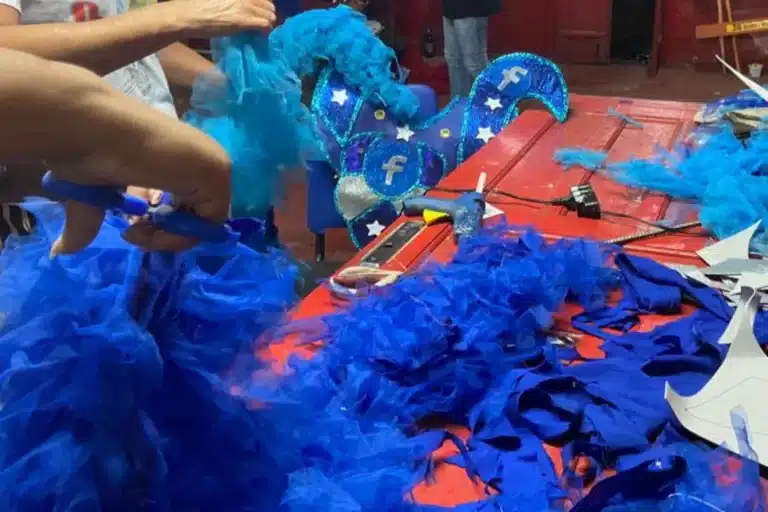 Costureira prepara uma fantasia vermelha, com plumas azuis, para o carnaval de 2023