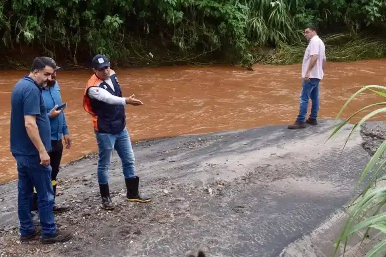 Pessoas observam o nível das águas e as margens de um rio.