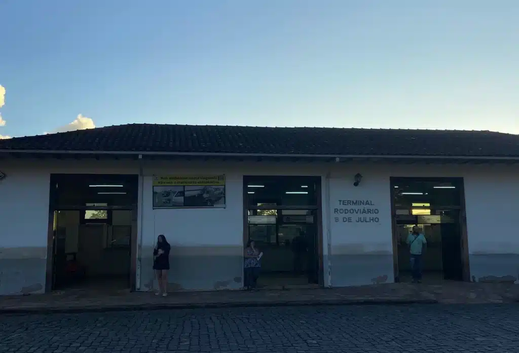 Pessoas aguardam para embarque em linhas municipais, em frente à fachada da rodoviária de Ouro Preto
