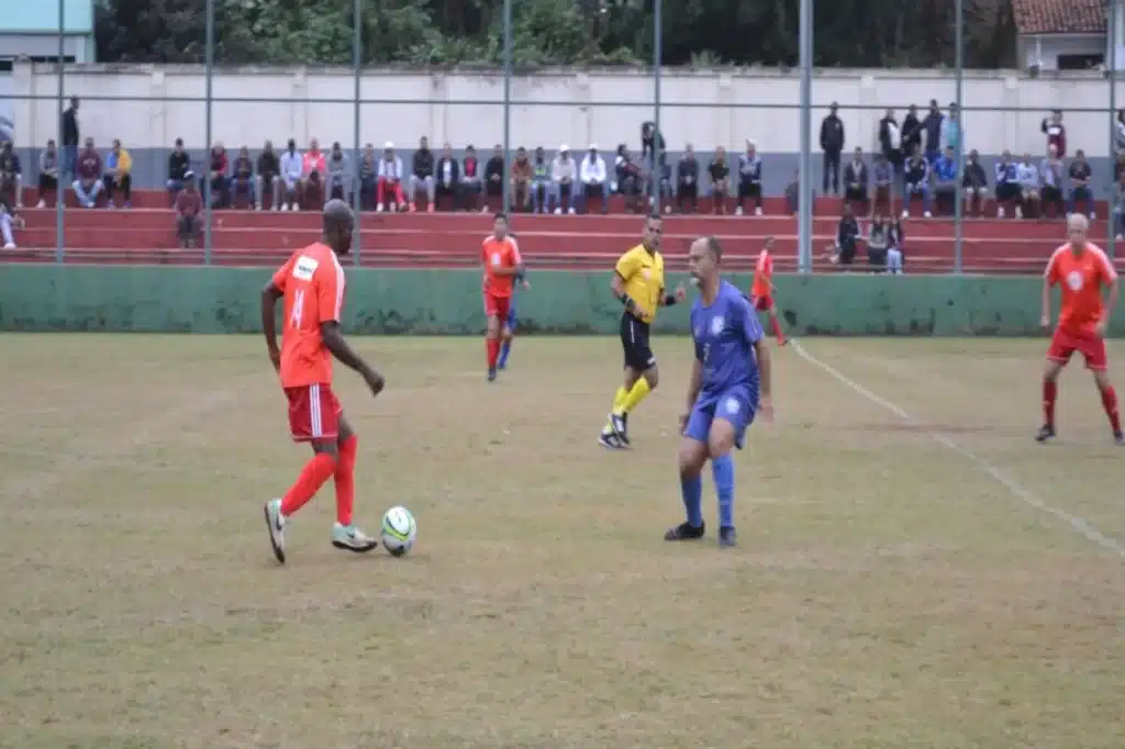 Atleta do Guarany (de vermelho) conduz a bola, marcado por jogador do Aluminas (de azul)