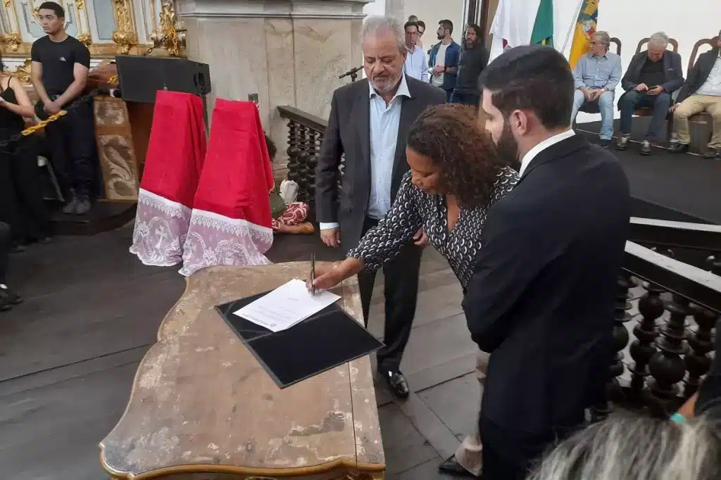 Ministra Margareth Menezes, ladeada por Celso Cota e Cristiano Vilas Boas, assina documento referente á convocação da Conferência Municipal de Cultura