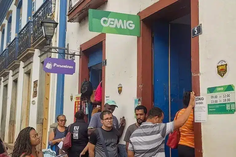 diversas pessoas fazem fila na porta de uma papelaria onde também acontece o atendimento da Cemig, em Mariana.