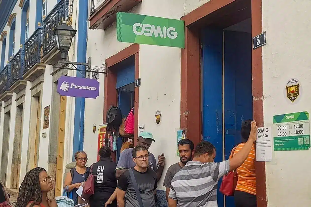 diversas pessoas fazem fila na porta de uma papelaria onde também acontece o atendimento da Cemig, em Mariana.