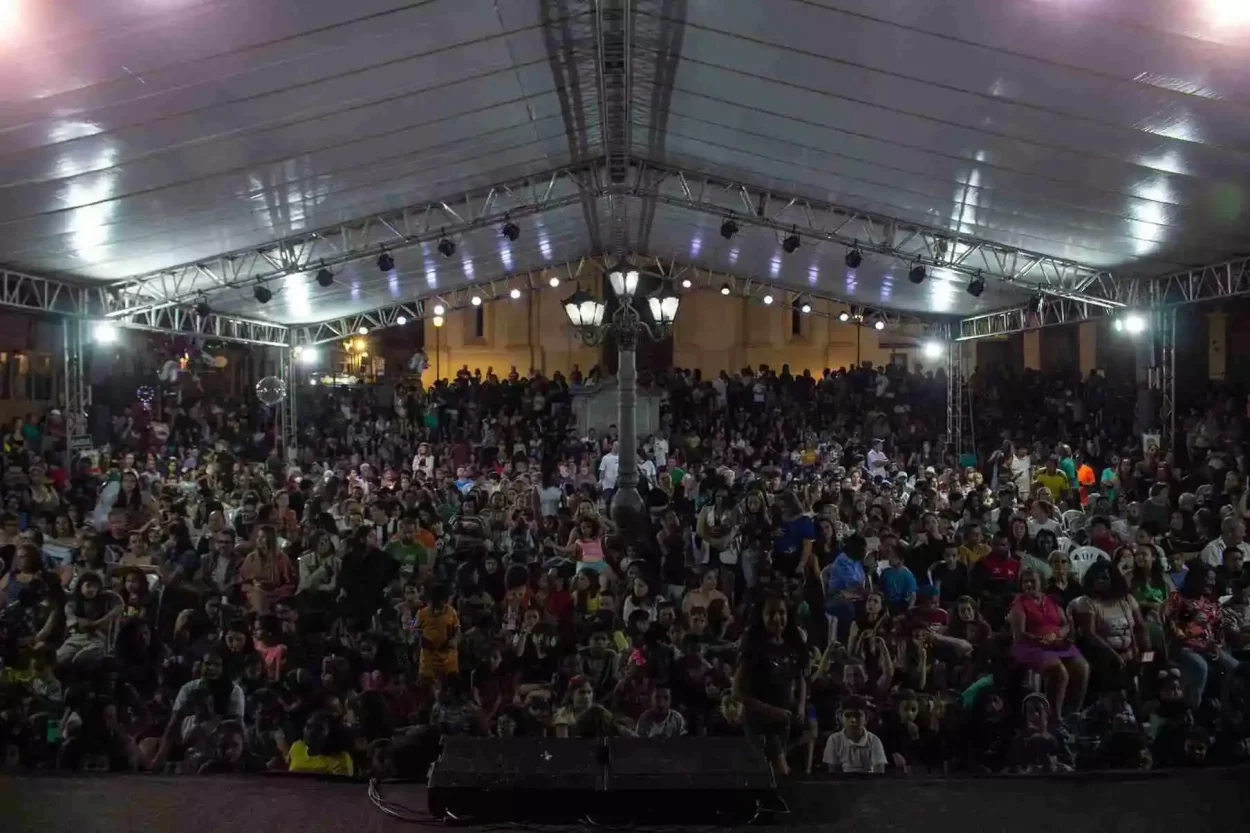 Multidão sob tenda iluminada assiste a espetáculo noturno do Circovolante ao ar livre.