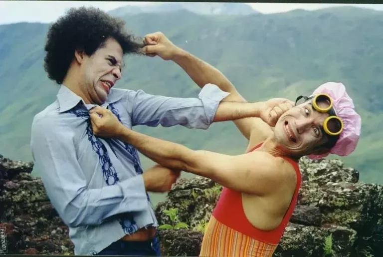 Dois palhaços do Circovolante encenam briga cômica com caretas e figurino colorido em meio à natureza.