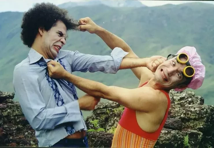 Dois palhaços do Circovolante encenam briga cômica com caretas e figurino colorido em meio à natureza.