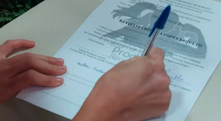 Mão feminina assina documento de participação no Programa Inclusão Produtiva, novo Mariana D’Elas.