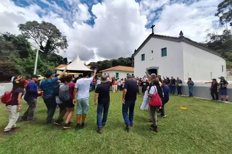 Peooas de mão pro alto em riste dançam em roda em frente a Capela de Santo Amaro