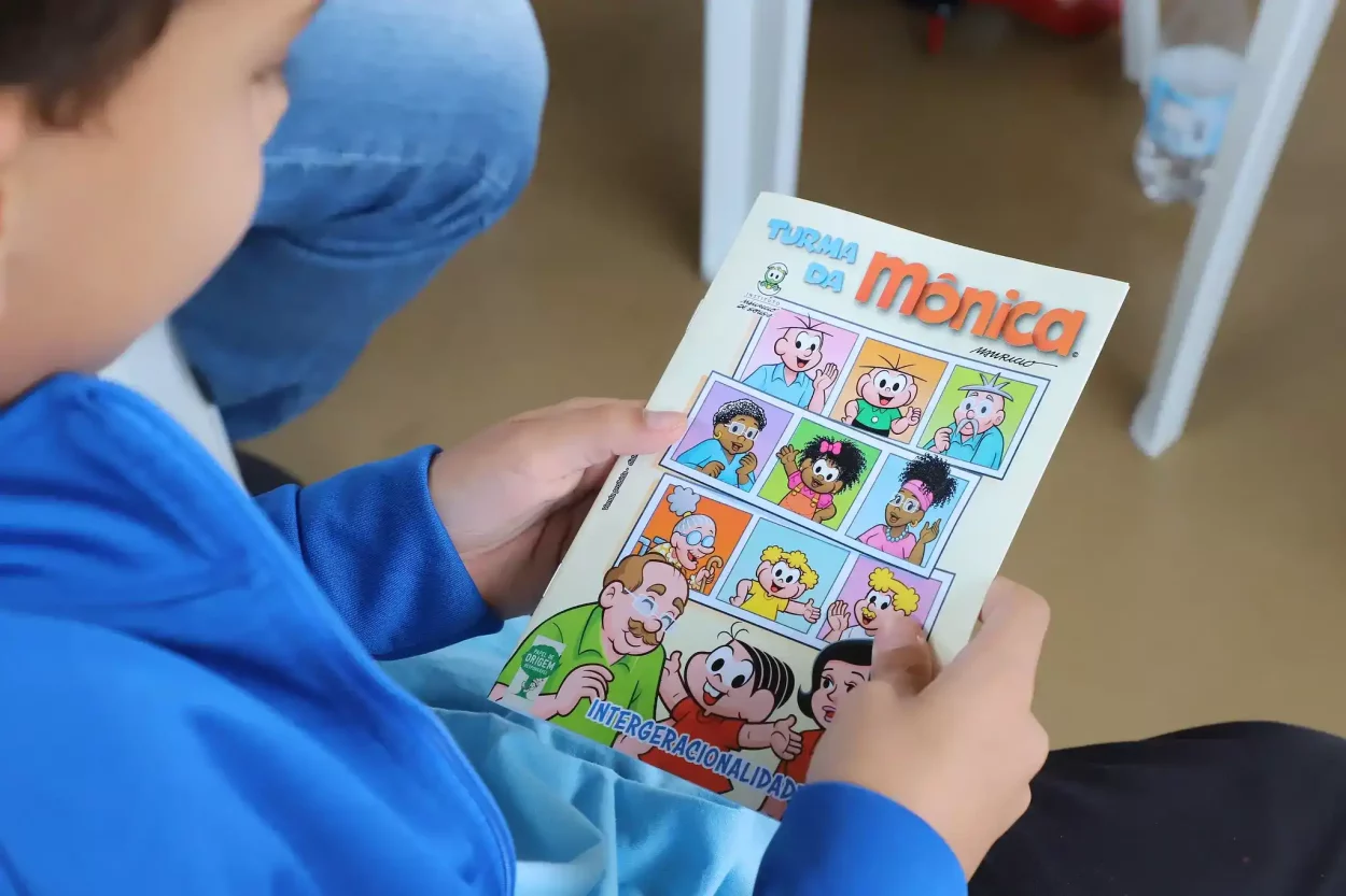 Criança segura revista “Turma da Mônica em: Intergeracionalidade”, com capa colorida que destaca o tema da convivência entre gerações.