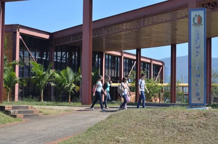 Estudantes caminhando em frente ao prédio moderno da Escola de Minas da UFOP no campus Morro do Cruzeiro.