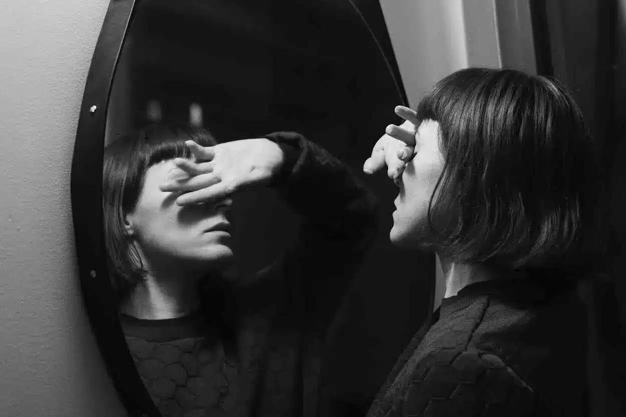 Mulher, diante do espelho, evita ver seu reflexo