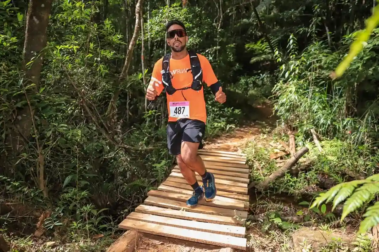 Corredor participa do Iron Runner em Mariana, correndo sobre uma ponte de madeira em meio à mata fechada.