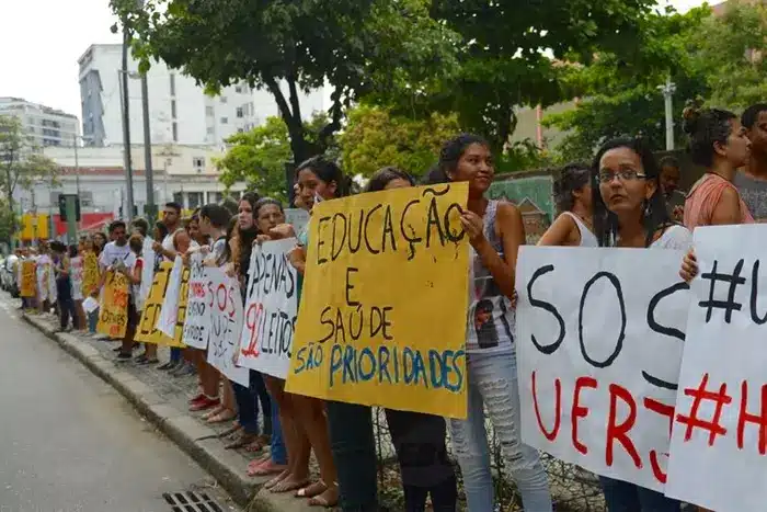 Manifestantes seguram cartazes pedindo prioridade para educação e saúde durante protesto em via urbana, destacando demandas que impactam diretamente o Índice de Desenvolvimento Humano (IDH).