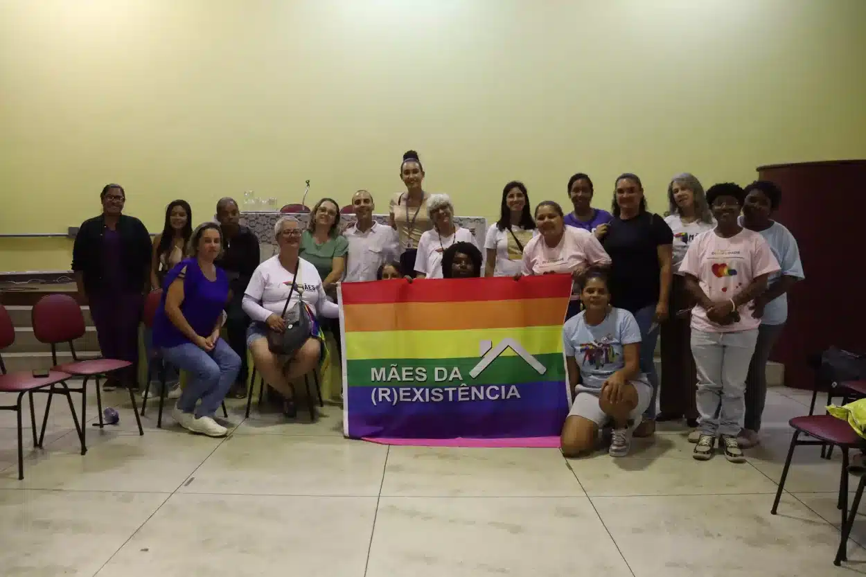 Grupo segurando uma bandeira colorida com o nome "Mães da (R)Existência" após palestra da semana da diversidade.