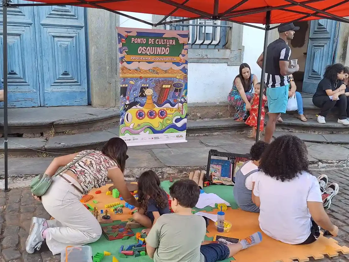 Crianças e adultos brincam com blocos de montar sob uma tenda na Semana Mundial do Brincar.