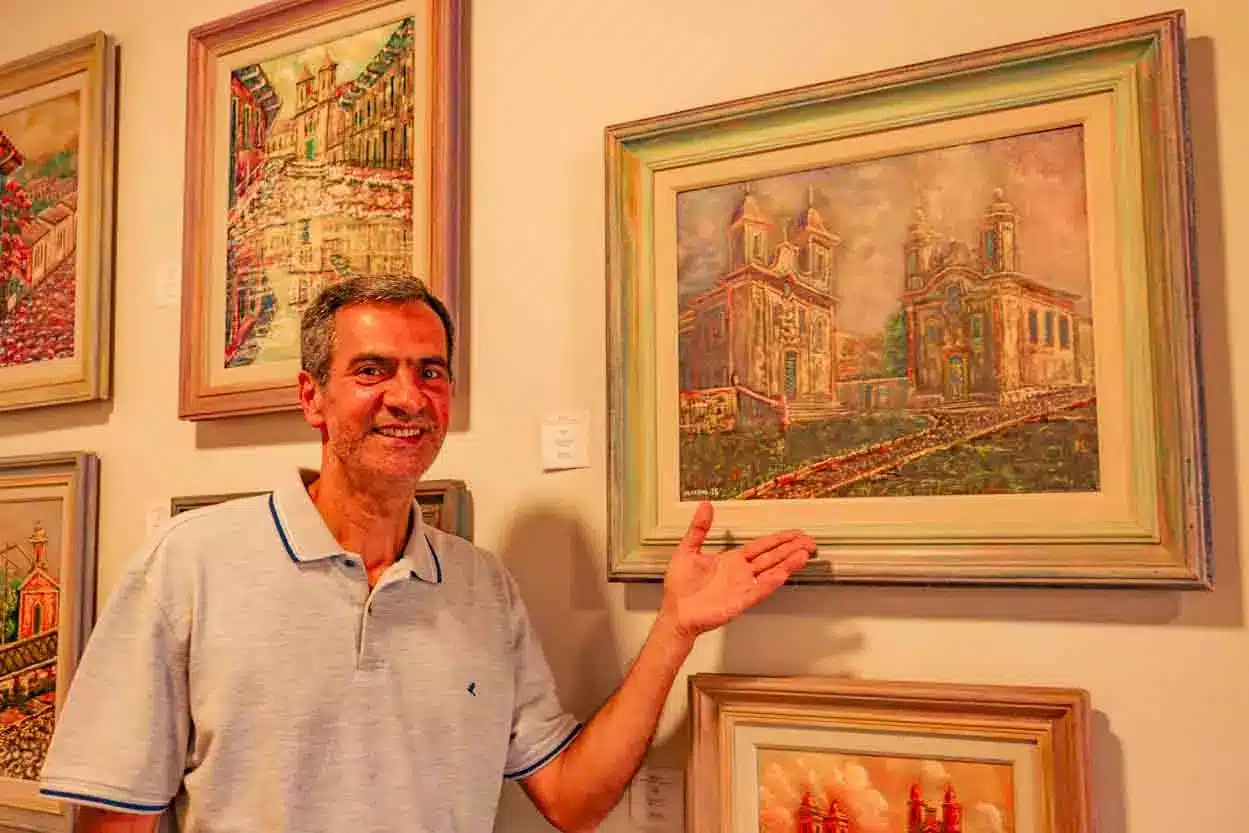 Na foto o pintor sorri ao mostrar uma de suas obras durante o projeto Ateliê Aberto.