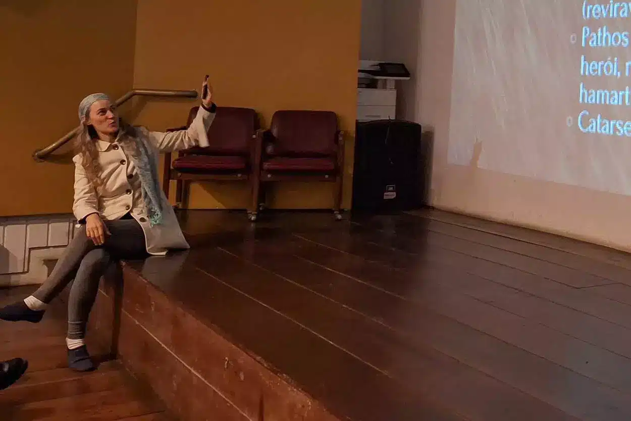 Mulher sentada no palco falando sobre cinema indígena.