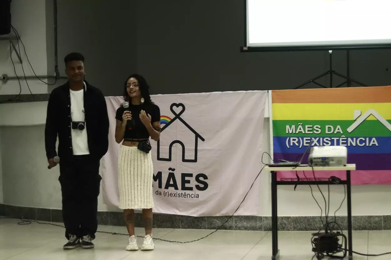 Marcos Vinícius e Aléxia Leles, diretores do documentário, apresentam o filme ao lado da bandeira do coletivo.