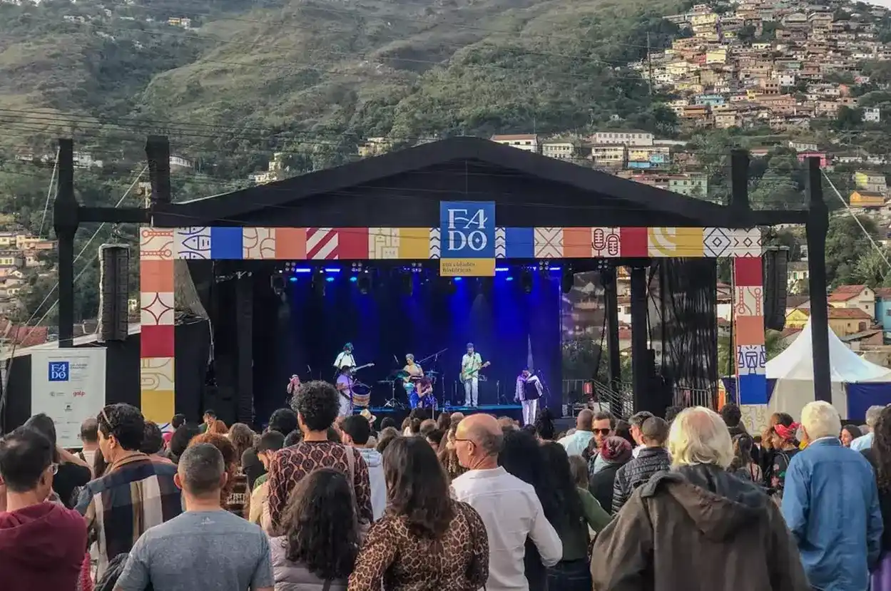 Público assiste a apresentação no palco do Festival Fado em Cidades Históricas em Ouro Preto, cercado por montanhas e casas históricas.