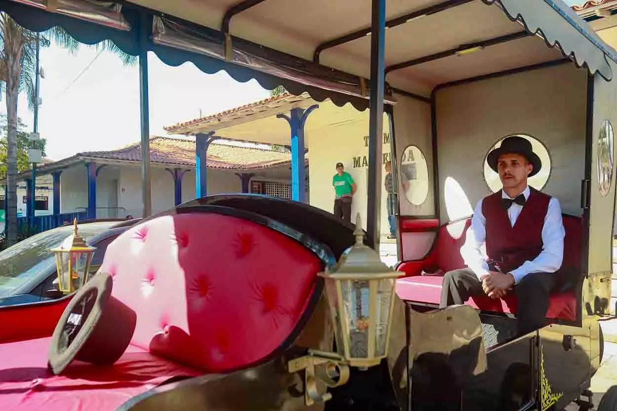 O cocheiro está dentro da charrete, sentado no banco de trás enquanto aguarda a chegada de passageiros, a charrete está estacionada no Terminal Turístico.