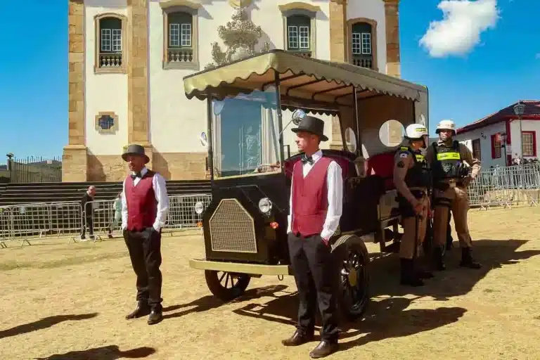 dois condutores em pé ao lado de uma charrete elétrica, estacionada no gramado da Praça Minas Gerais, ao lado vemos dois policiais militares encostados no veículo.