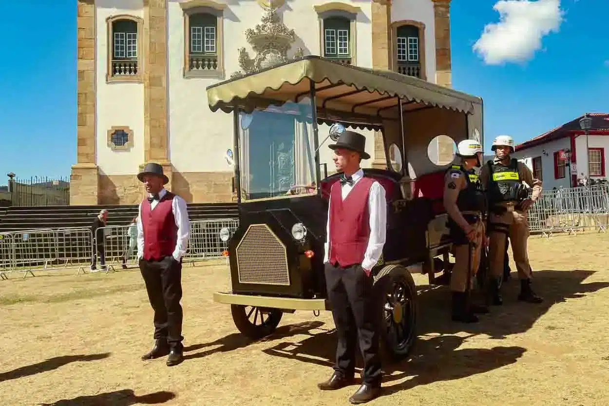 dois condutores em pé ao lado de uma charrete elétrica, estacionada no gramado da Praça Minas Gerais, ao lado vemos dois policiais militares encostados no veículo.