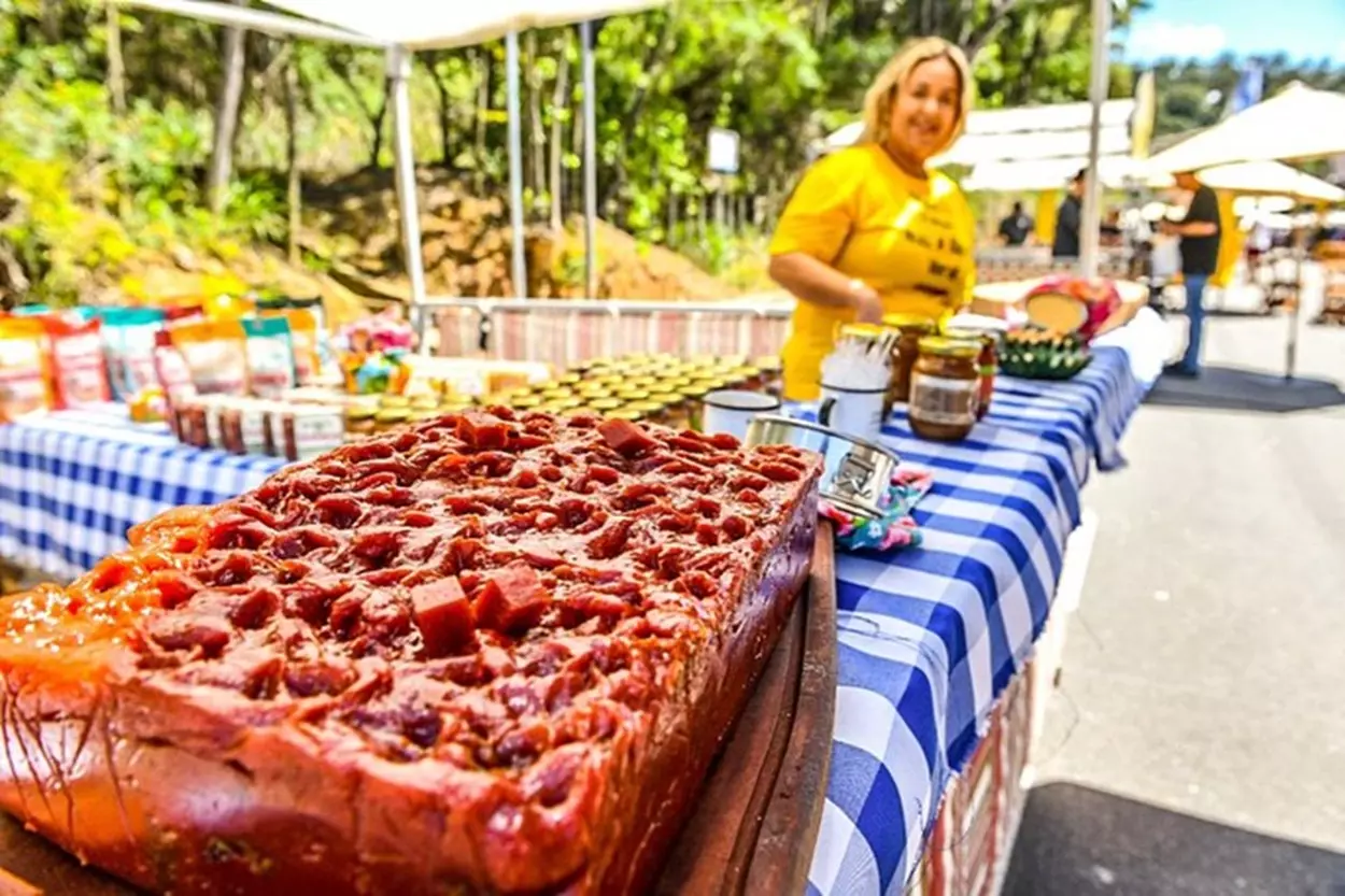 Na foto em se vê uma travessa de doce e uma mulher em uma barraquinha da feira.