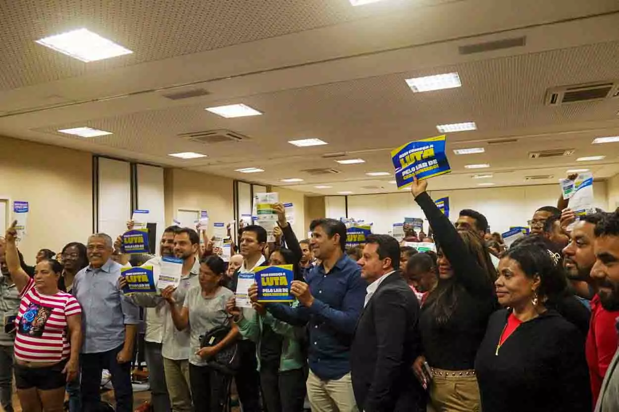 Prefeito e vários políticos locais seguram cartazes pra cima em comemoração do minha casa, minha vida