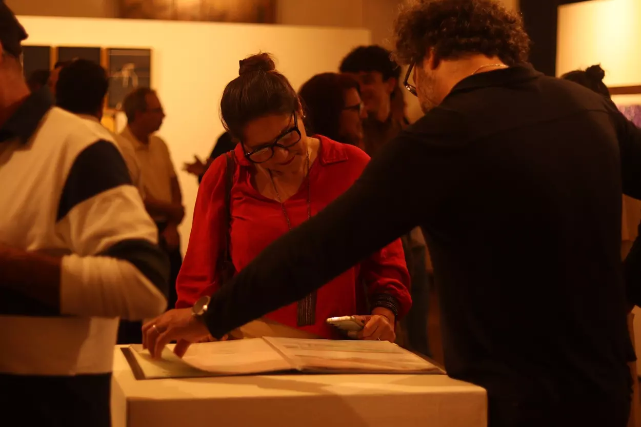 Visitantes folheiam caderno de Desenho e Aquarela feito pelos moradores locais, pensado pelo arquiteto André Perdigão, exposto da Mostra Desvia, que corrobora para a ideia de representatividade levada pela exposição em Ouro Preto. - Foto: Joyce Campolina/Agência Primaz
