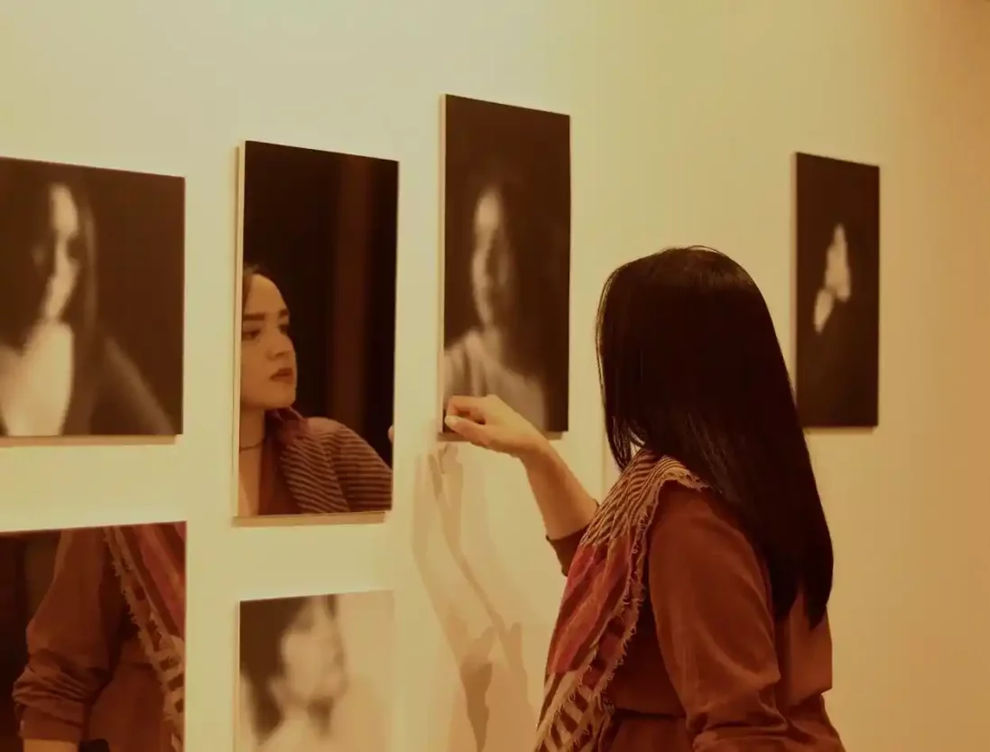 Fotógrafa Mila Damasceno em frente ao seu projeto interativo na exposição Desvia em Ouro Preto. Ela brinca entre o ato de se ver no espelho e intercalar esse olhar as imagens desfocadas presentes em seu quadro. Foto: Joyce campolina/Agência Primaz